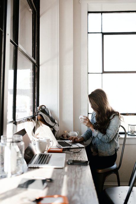 Frau trinkt Kaffee auf der Arbeit vor dem Laptop